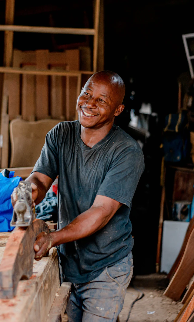 Carpintero sonriendo mientras cepilla una tabla en su taller