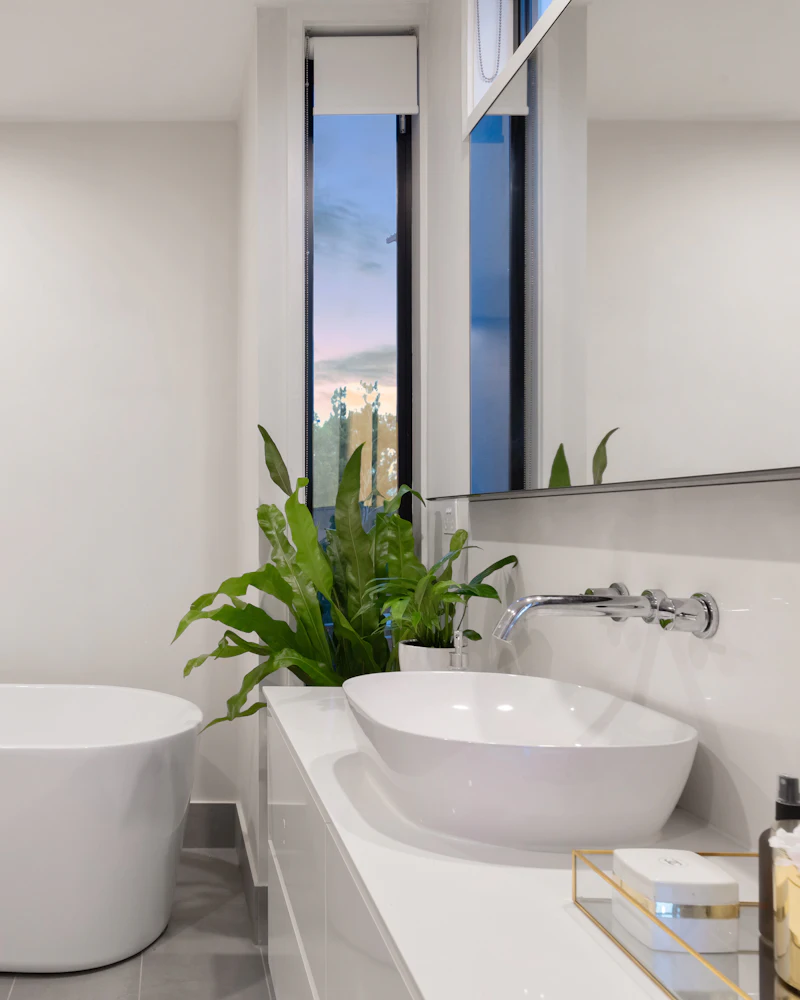 Baño renovado con tina blanca y una planta junto a la ventana