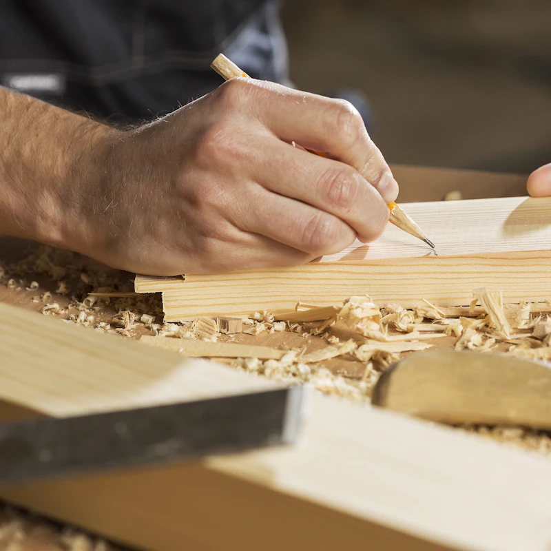Mano marcando con lápiz una línea sobre una tabla de madera